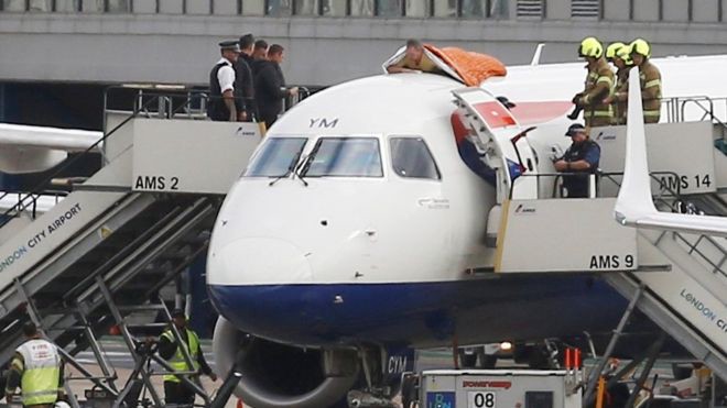A man lies on top of a jet aircraft at London City Airport